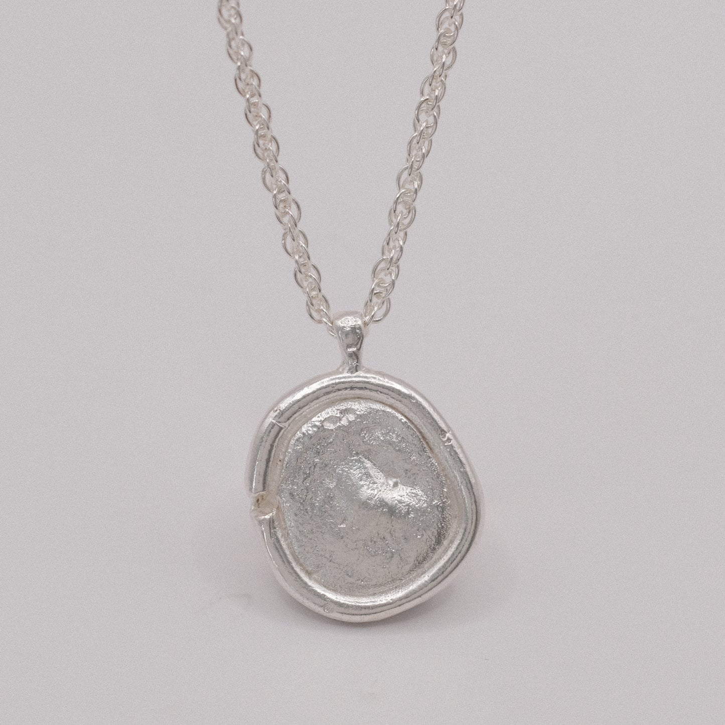 Silver necklace with a textured pendant resembling an ancient coin