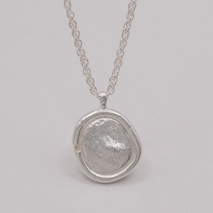 Silver necklace with a textured pendant resembling an ancient coin