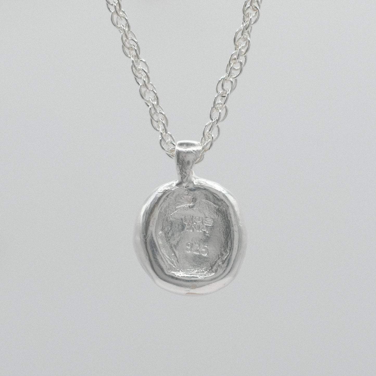 the back of a sterling silver necklace featuring a textured, hammered circular pendant suspended from a delicate double anchor chain