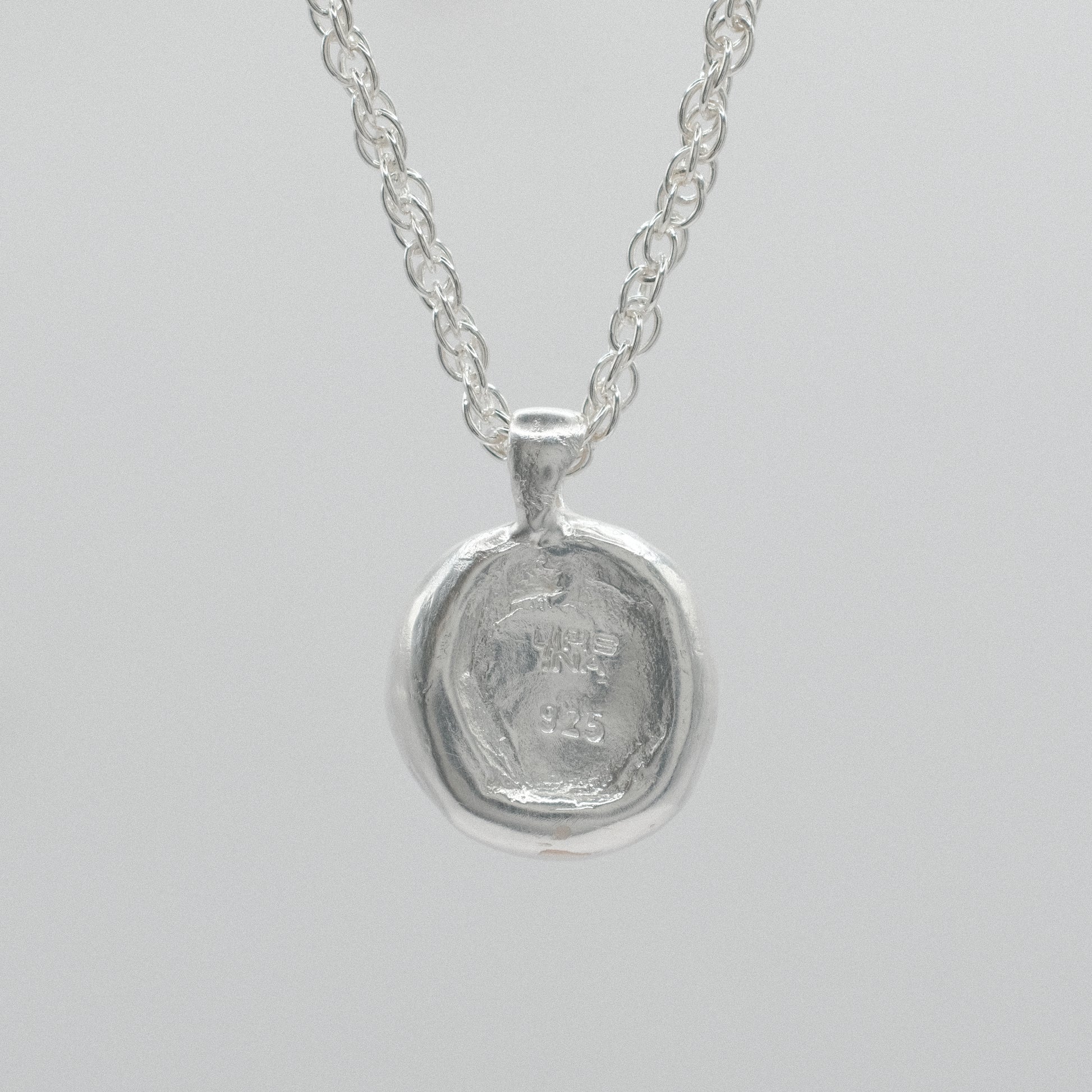 the back of a sterling silver necklace featuring a textured, hammered circular pendant suspended from a delicate double anchor chain