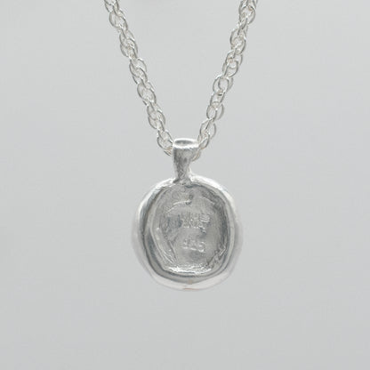 the back of a sterling silver necklace featuring a textured, hammered circular pendant suspended from a delicate double anchor chain
