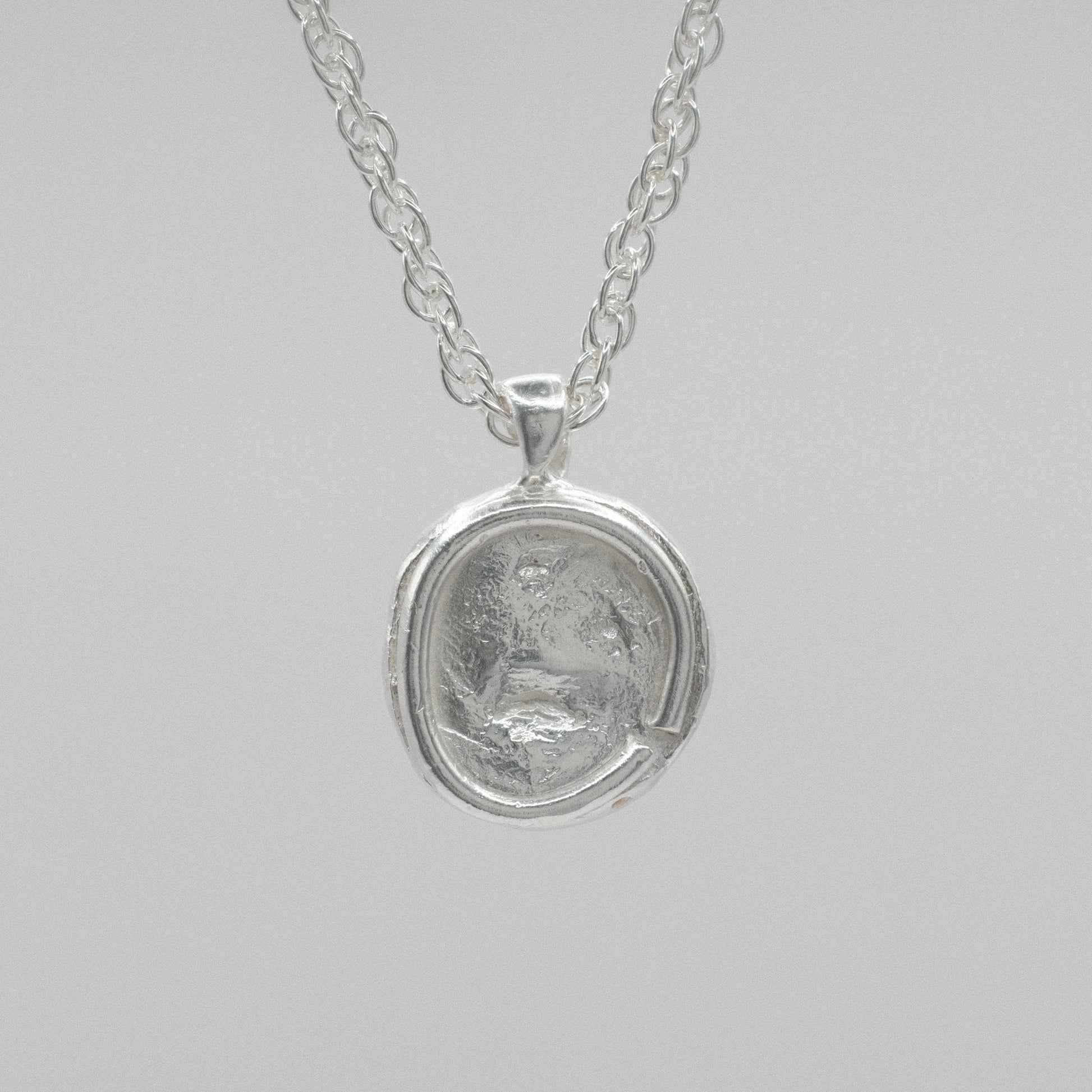 A silver pendant necklace featuring a circular, textured coin-like medallion pendant on a delicate silver chain