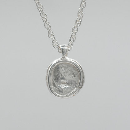 A silver pendant necklace featuring a circular, textured coin-like medallion pendant on a delicate silver chain