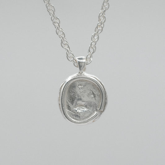 A silver pendant necklace featuring a circular, textured coin-like medallion pendant on a delicate silver chain