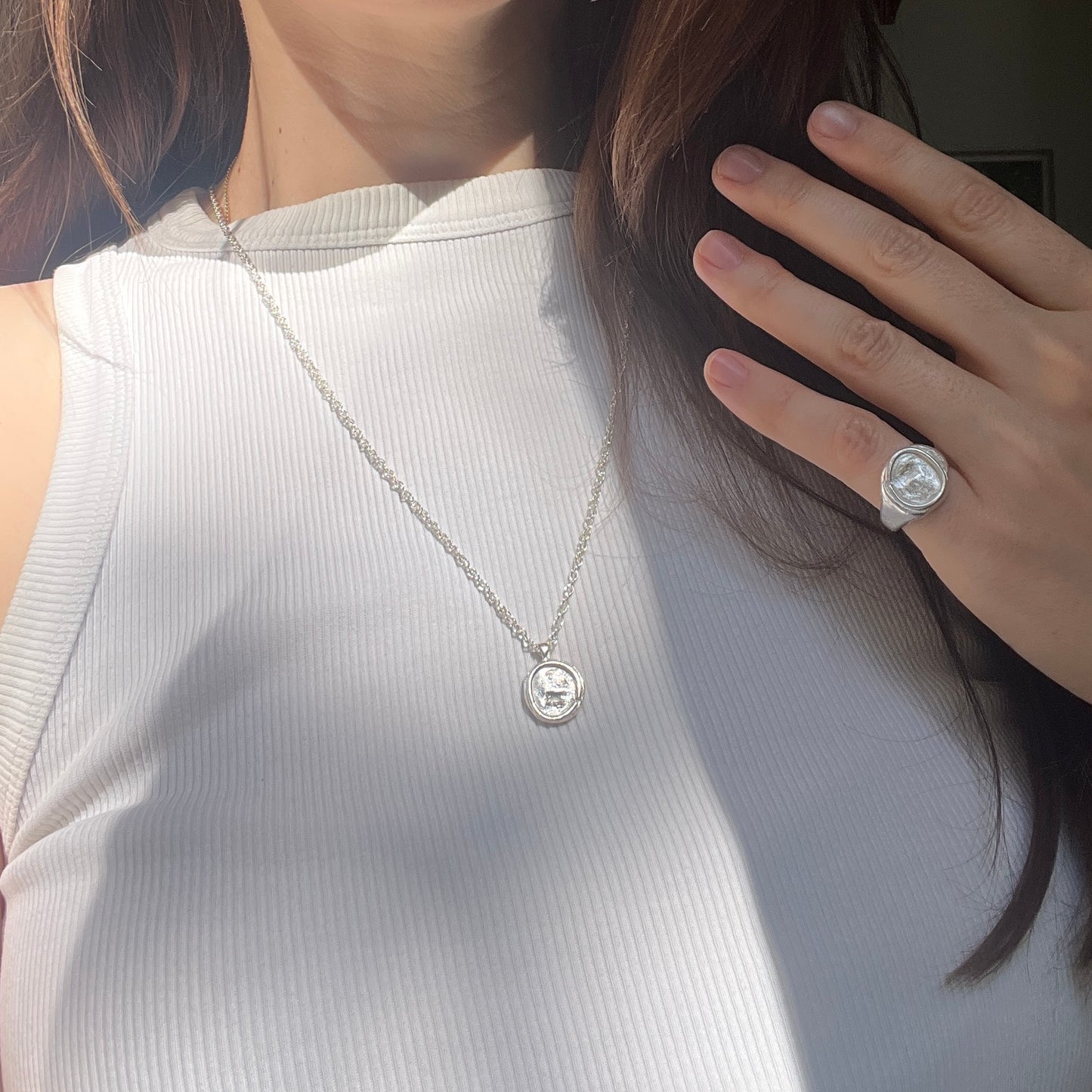A close-up lifestyle shot of a woman wearing a silver chain coin necklace with a round pendant and a silver coin ring 